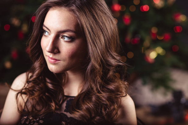 Portrait of young brunette woman in a black dress over christmas background - Fotoğraf, Görsel