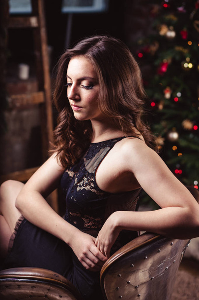 Portrait of young brunette woman in a black dress over christmas background - Foto, imagen