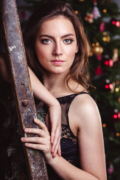 Portrait of young brunette woman in a black dress over christmas background - Fotoğraf, Görsel