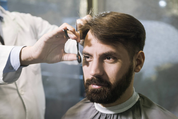 Front view of a bearded businessman having his hair cut in a barber shop. - Foto, Imagem