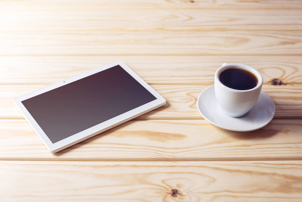 digital tablet lying on wooden table and cup of coffee - Foto, afbeelding