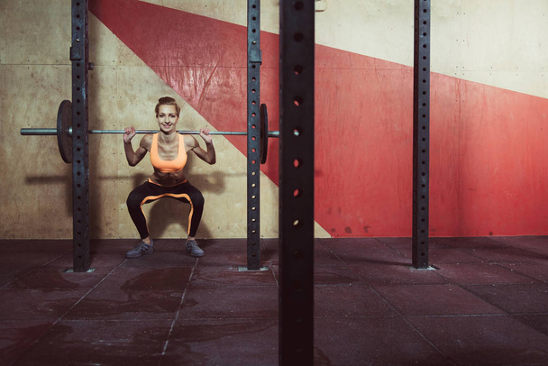 Gym. She squats with a barbell - Zdjęcie, obraz