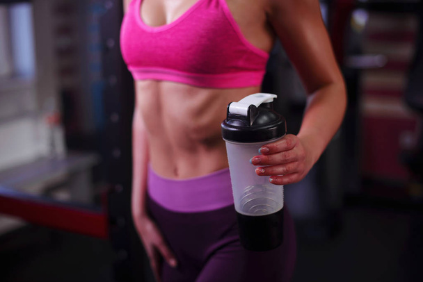 The sports young woman with protein cocktail in a shaker in a gym. Sports nutrition concept - Foto, Bild