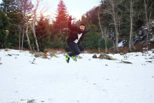 若い男のコートと手袋を身に着けているジャンプと雪を楽しむ - 写真・画像