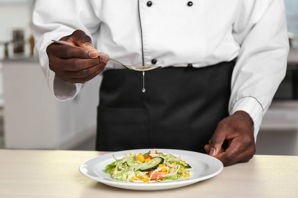 African American chef cooking tasty salad in kitchen, closeup - Foto, afbeelding