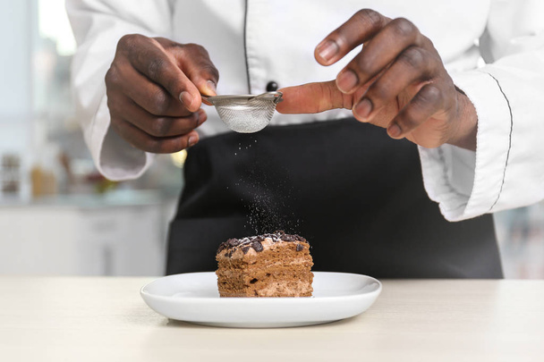 African American chef sifting sugar on tasty cake in kitchen, closeup - Foto, afbeelding