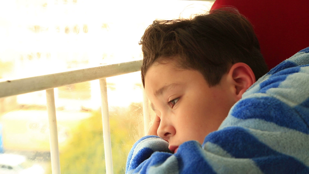 Ένα νεαρό αγόρι κάθεται κοιτάζοντας έξω από το παράθυρο - Πλάνα, βίντεο