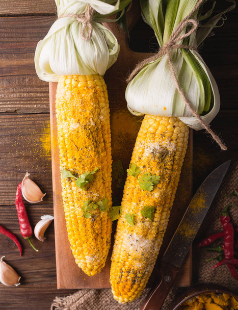 Boiled corn with salt, parmesan, herbs, chili peppers on a wooden background - Fotografie, Obrázek