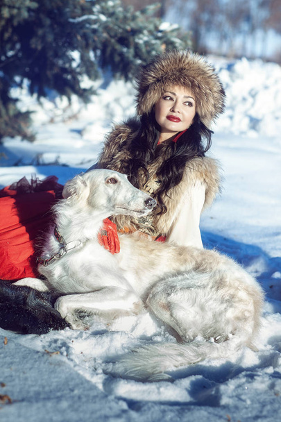 girl a fur vest and red skirt lying with dog in the snow - Foto, afbeelding