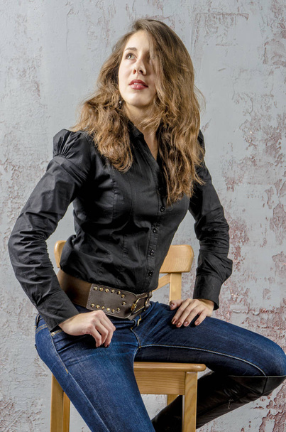  Young girl with curly hair in a black shirt, jeans and high boots cowboy western style - Фото, изображение