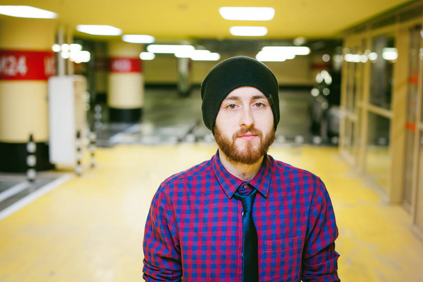 portrait of a man with a beard in a plaid shirt and a tie and hat, underground parking - Foto, immagini