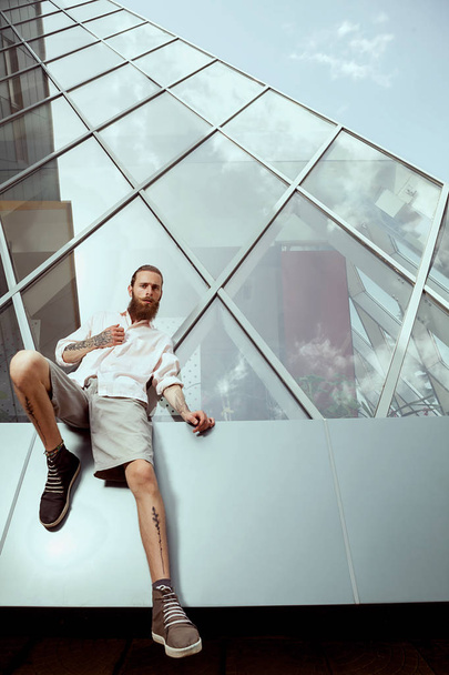 Hipster mit langem Bart und Tätowierungen vor Bürogebäude - Foto, Bild