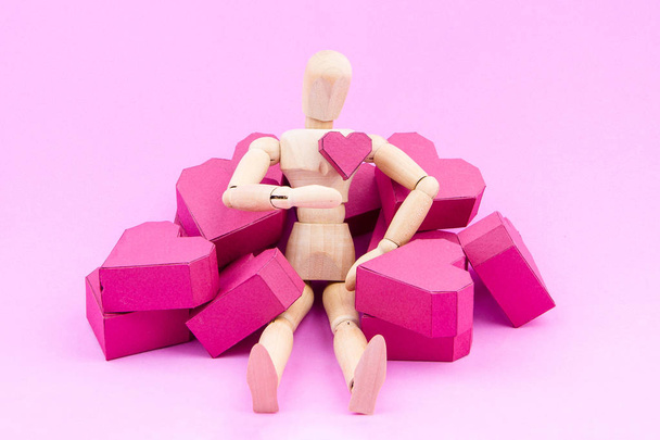 Wooden dummy and a pile of paper box red heart shape on pink bac - Фото, изображение