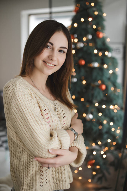 Portrait of lovely woman in pullover at christmas tree background - Foto, imagen