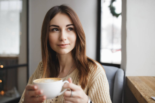 Woman sitting with cup of coffee in a cafe and look at window - Фото, изображение