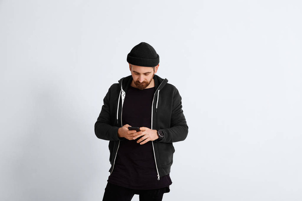 Young man in black looking on his smartphone - Foto, Imagen
