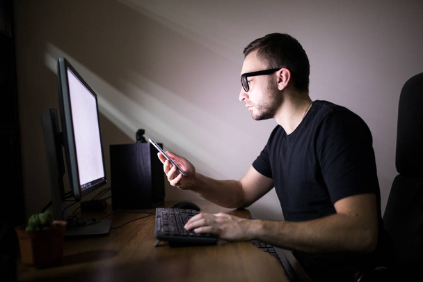 Mies käyttää puhelinta lähellä PC
 - Valokuva, kuva