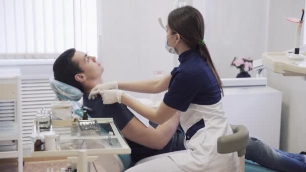 beautiful female dentist prepares the patient to the procedures in the dental clinic, puts on chest sterile cloth. Concept of heatlhy life - Кадри, відео