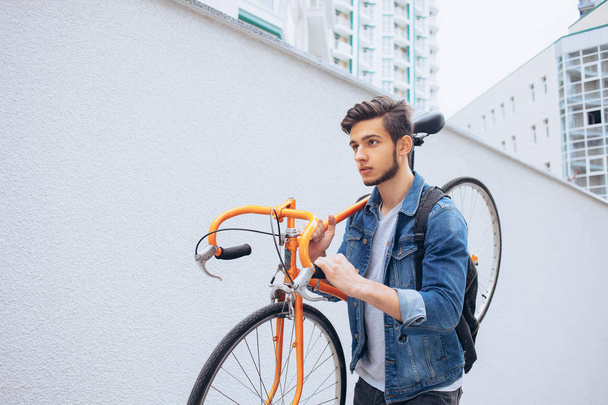 The guy in the blue jeans jacket carries on his shoulder orange bike. A young man on an orange fix bike - Foto, Bild