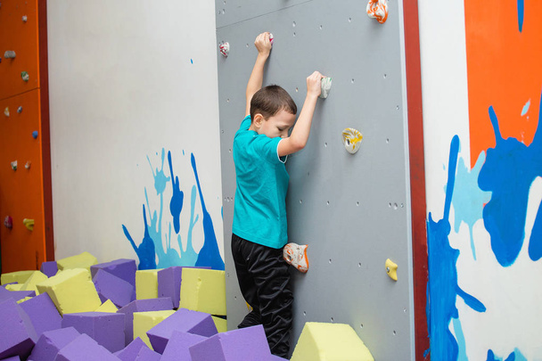 little active boy 7 year old rock climbing at indoor gym artificial wall - Foto, afbeelding