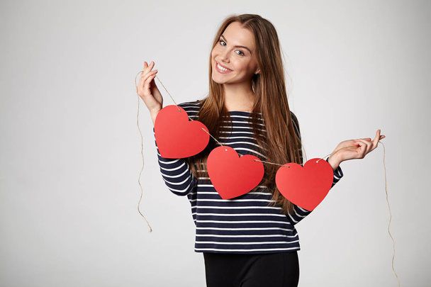 Smiling woman holding garland of five red paper hearts - Foto, immagini