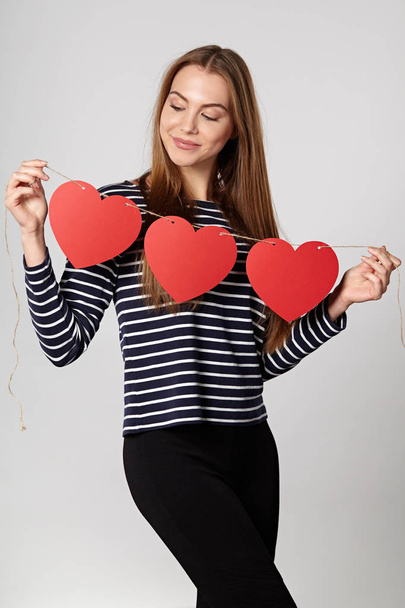 Smiling woman holding garland of three red paper hearts - Foto, Bild