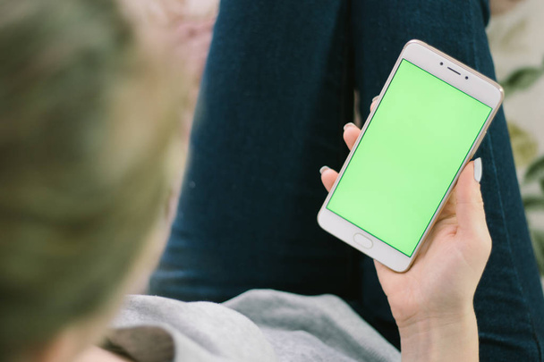 schönes Mädchen hält ein Smartphone in den Händen eines grünen Bildschirms, die Hand des Mannes hält ein Mobiltelefon mit Chromaschlüssel, grüner Bildschirm auf weißem Hintergrund, neues Technologiekonzept - Foto, Bild