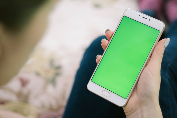 schönes Mädchen hält ein Smartphone in den Händen eines grünen Bildschirms, die Hand des Mannes hält ein Mobiltelefon mit Chromaschlüssel, grüner Bildschirm auf weißem Hintergrund, neues Technologiekonzept - Foto, Bild