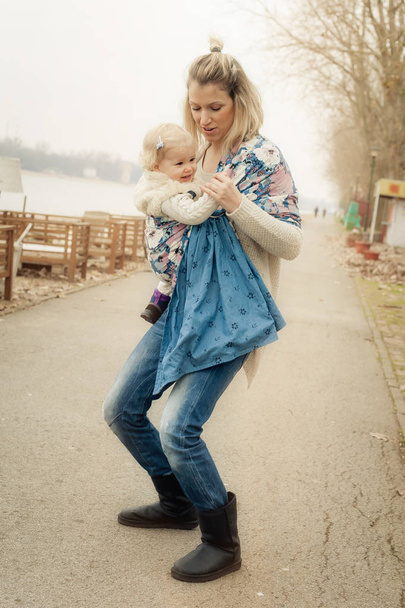 Young mother having her little daughter in baby carrier scarf - Fotografie, Obrázek