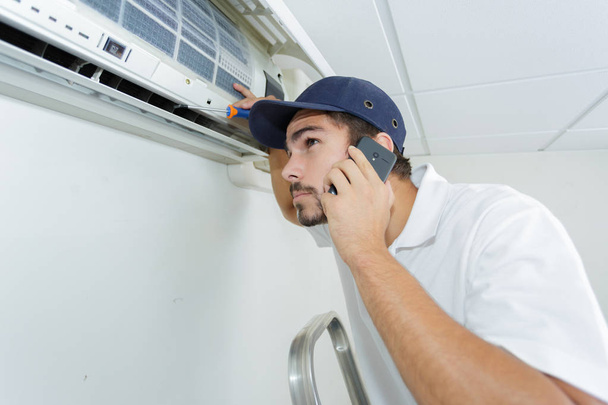 young handyman repairing air conditioning system calling for help - Fotoğraf, Görsel