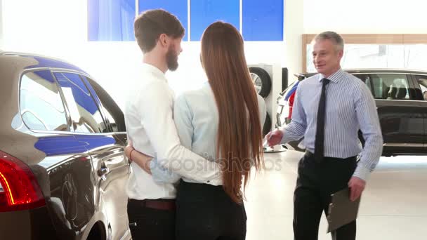 Πωλητής συμβουλεύεται νεαρό ζευγάρι στην αντιπροσωπεία αυτοκινήτων - Πλάνα, βίντεο