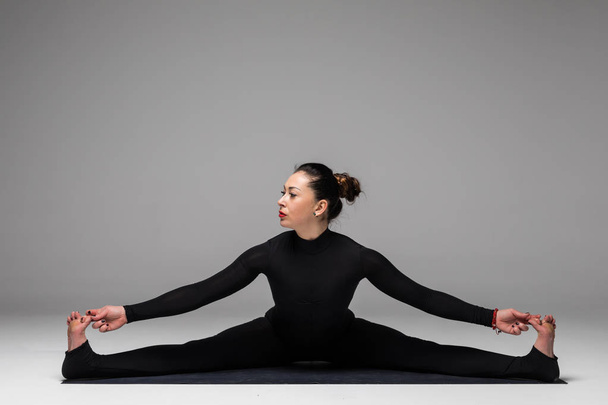 Hermosa mujer de yoga en santa hat práctica yoga posa sobre fondo gris
.  - Foto, Imagen
