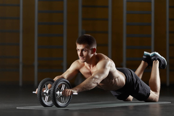 Man doing sport exercise on floor with toning wheel - 写真・画像