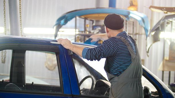 Professioneller Autoservice - ein Arbeiter poliert blaues Auto - Foto, Bild