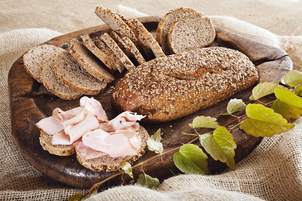 integral bread on the wood board with ham and green branch, note shallow depth of field - 写真・画像