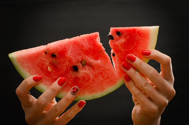 Hibás nagy szelet görögdinnye érett női kezek-ra egy fekete háttér, közelkép - Fotó, kép