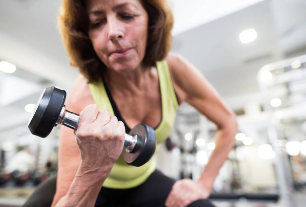 Senior woman in gym working out with weights. - Zdjęcie, obraz