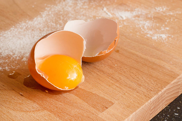 Закрыть яйцо, желток в яичной скорлупе, мука на деревянном фоне
 - Фото, изображение
