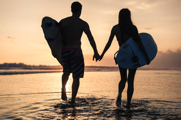 Couple of surfers over sunset on coastline - Фото, изображение