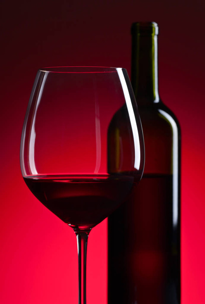 glass and bottle with red  wine on red background - Valokuva, kuva