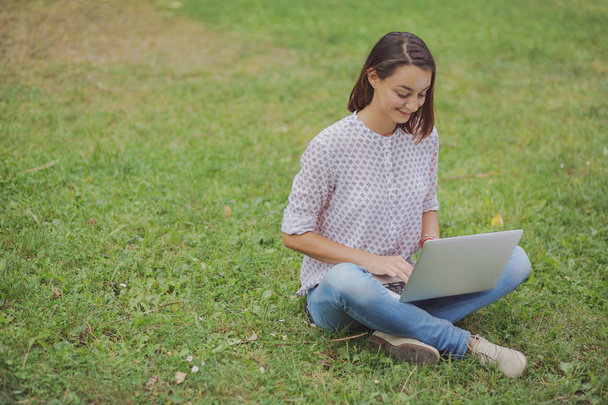 Young woman with laptop sitting on green grass - Photo, Image
