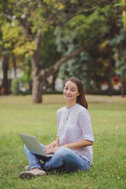 Young woman with laptop sitting on green grass - Fotó, kép