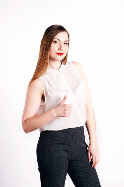 Beautiful young woman (girl) with long light brown hair in a white blouse standing straight and shows a hand sign of approval. White background. Portrait of the waist - Fotografie, Obrázek