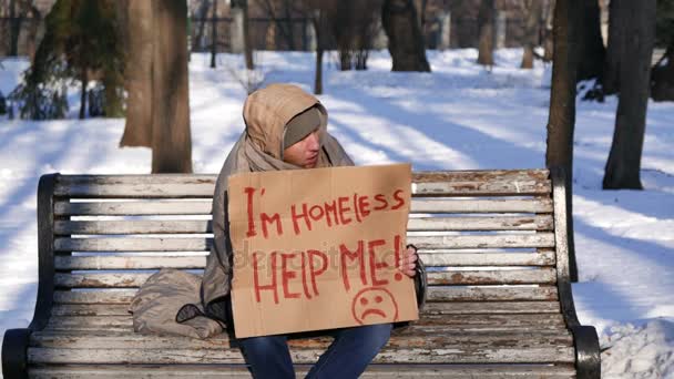  4 k. Freeze bezdomny młody człowiek z tektury siedzieć i prosić o pomoc w zimie miasto  - Materiał filmowy, wideo