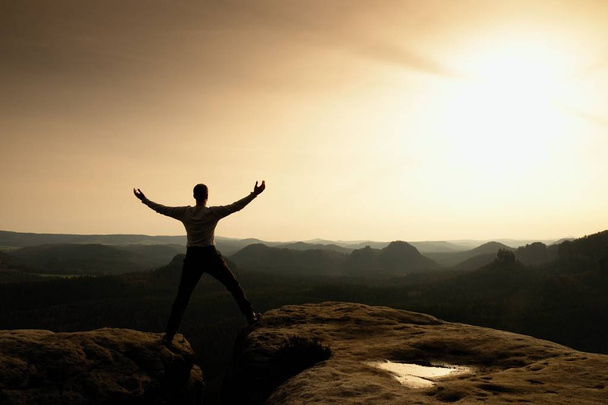 glückliche Mann mit erhobenen Armen Geste Triumph auf exponierter Klippe. Wanderer befriedigen Silhouette auf Sandsteinfelsen mit Blick auf hügelige Landschaft.  - Foto, Bild
