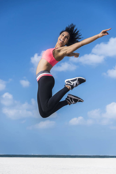 змішана гонка атлетична жінка в спортивному вбранні стрибає в сонячний день з блакитним небом і білими хмарами
 - Фото, зображення