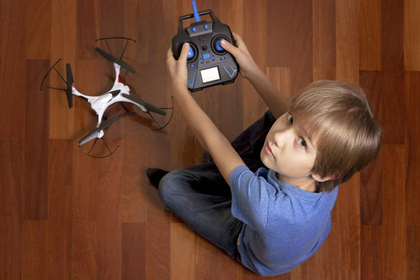 Małe dziecko będzie grać z quadcopter drone w domu. Chłopiec siedzi na podłodze i trzymając pilota radiowego - Zdjęcie, obraz