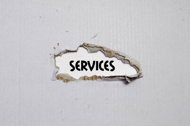 Das Wort Dienstleistungen taucht hinter zerrissenem Papier auf - Foto, Bild