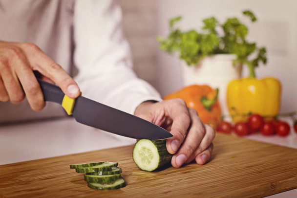 Chef's hands. Man is ready to prepare fresh salad. Chopping cucumber. - Foto, afbeelding