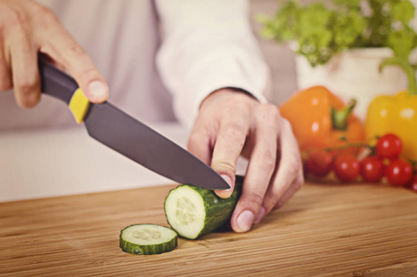 Chef's hands. Man is ready to prepare fresh salad. Chopping cucumber. - Фото, зображення